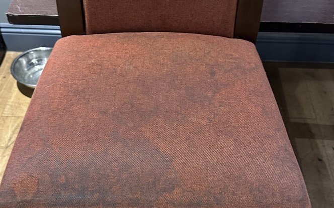 A venue bar chair before cleaning, the seat dark and mottled with years of ground-in dirt