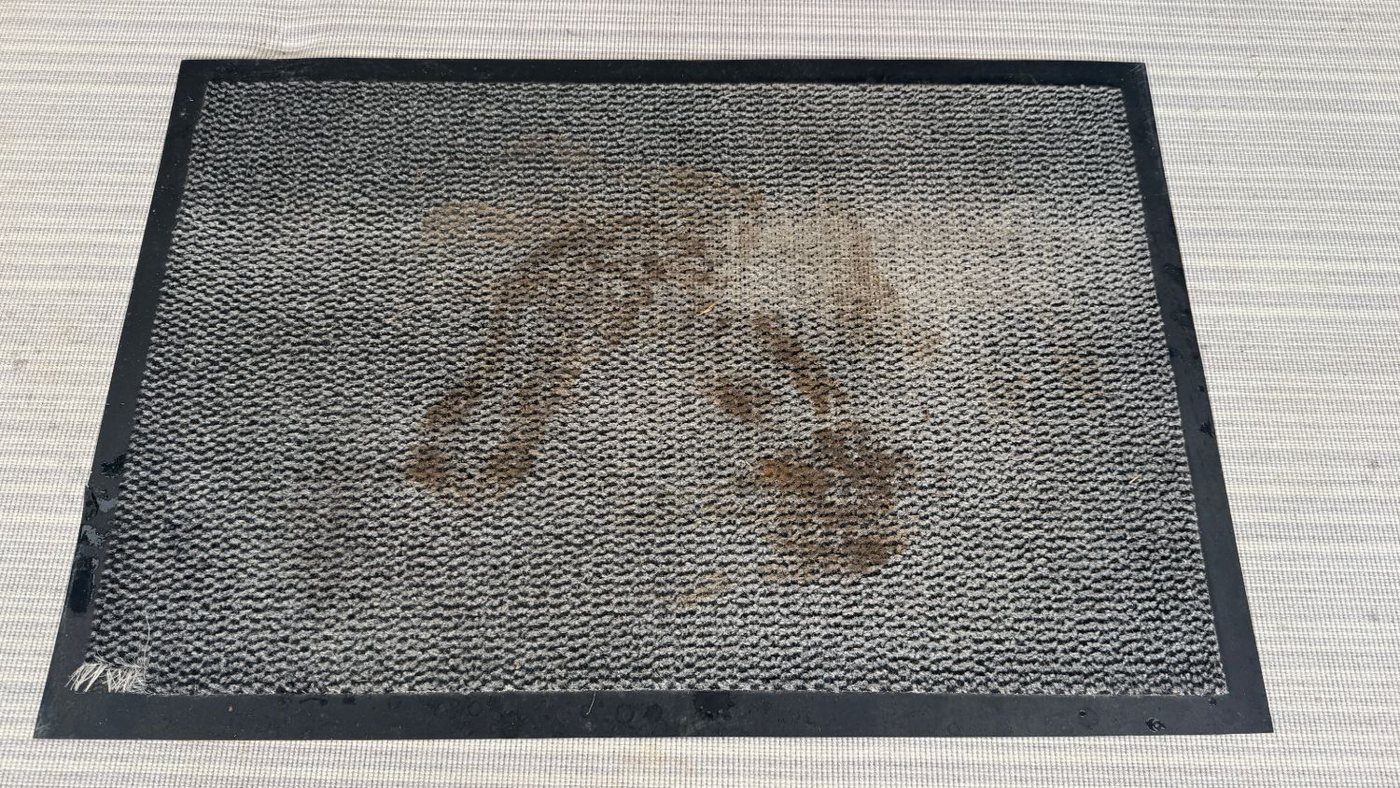 Muddy footprints on a grey door mat before cleaning