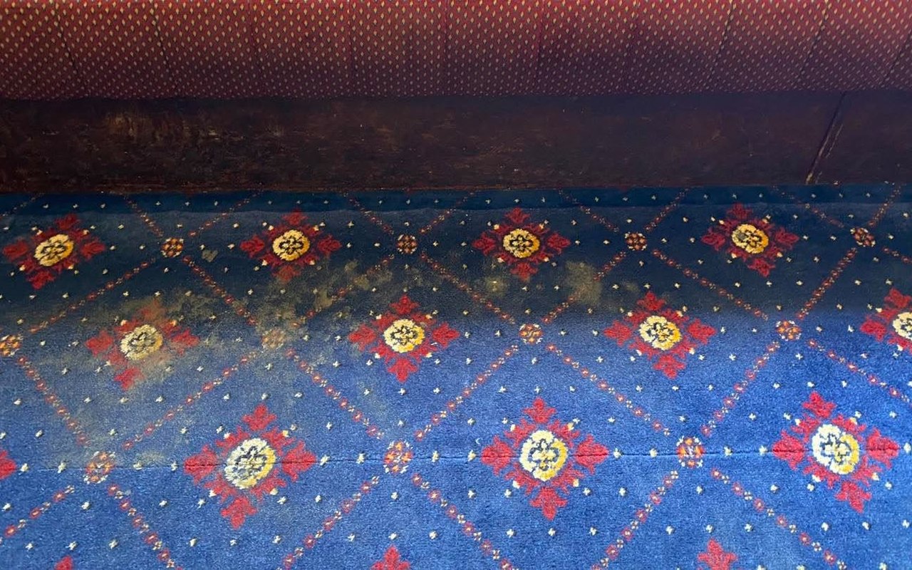 A patterned function-room carpet with a dark drink-stained patch before cleaning